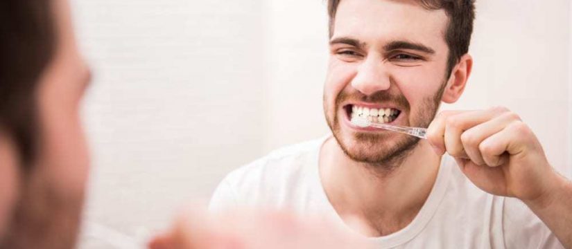 Young man looking in mirror while brushing his teeth